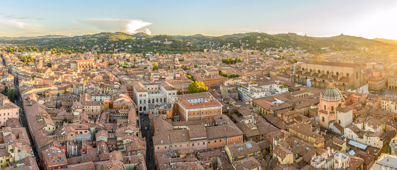 Bologna's red roofs from above at sunset, with the hills behind