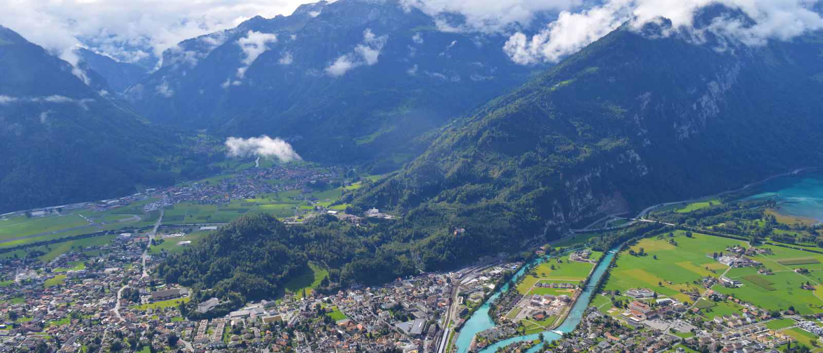 Interlaken from above: the town, the turquoise Aare and green meadows, with mountains in cloud behind
