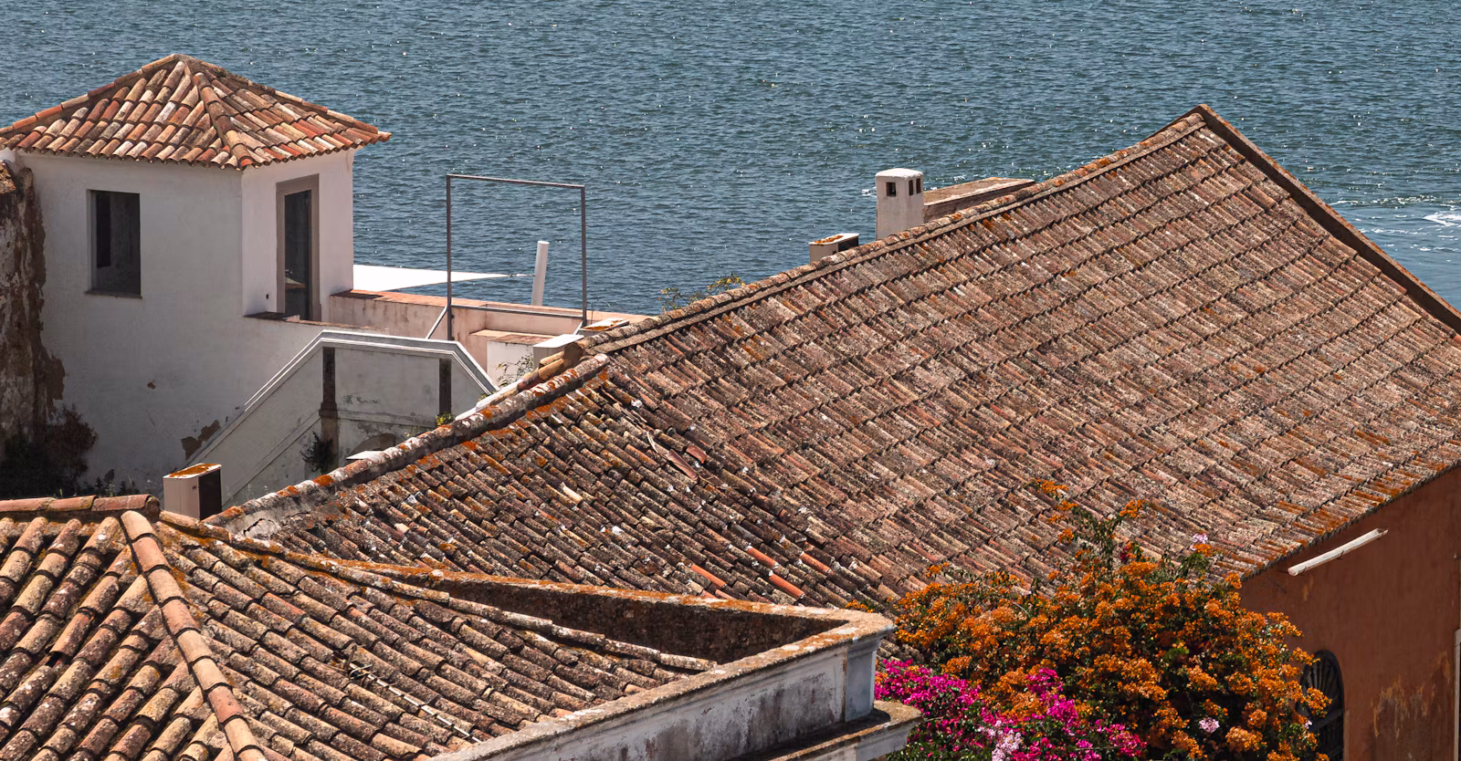 Old tiled roofs and bougainvillea in Faro, with the water of the Ria Formosa behind