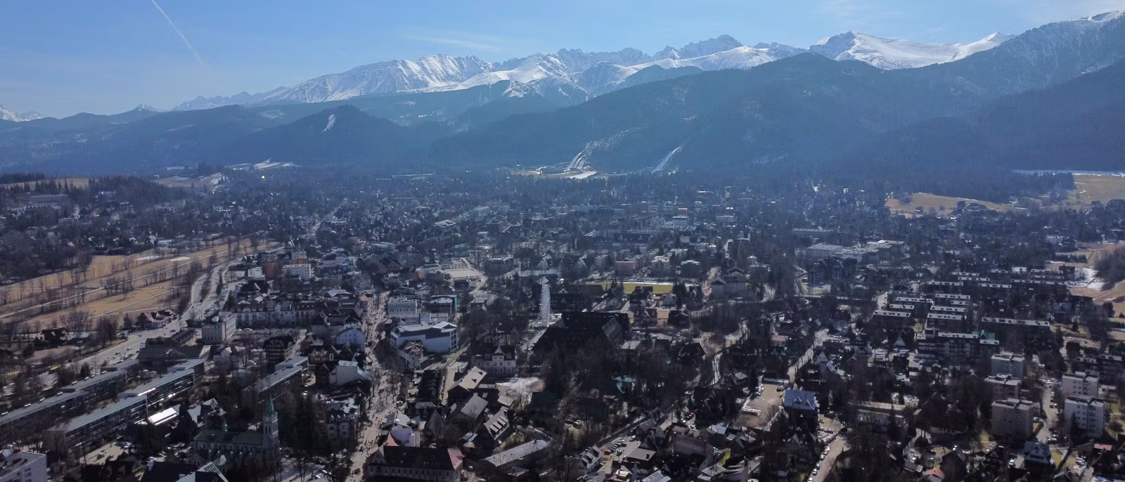 Zakopane from above in early spring, with the snow-capped Tatra ridge and the ski jump behind the town
