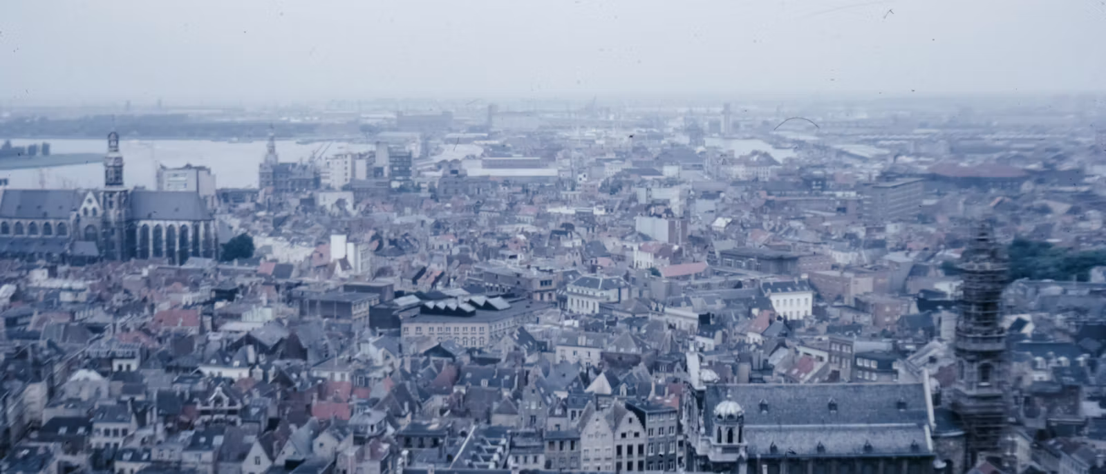 Slate roofs of old Antwerp from high above, with a Gothic church and the Scheldt beyond